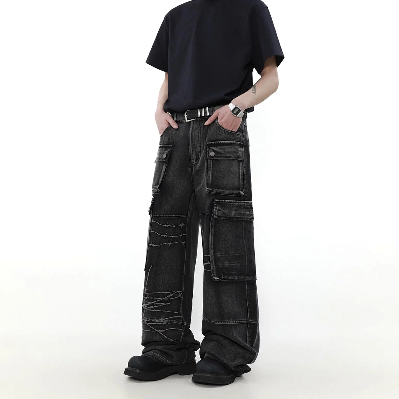 Side view of oversized washed black wide-leg cargo jeans featuring flap utility pockets, faded denim, and barbed wire embroidery
