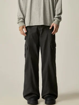 Black wide leg cargo pants shown from the front on a male model wearing a gray long sleeve shirt, featuring side utility pockets and a relaxed Korean streetwear silhouette