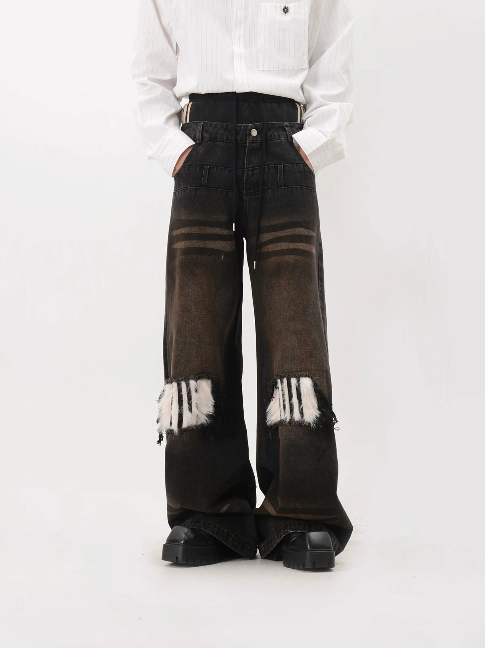 Front view of oversized wide leg streetwear jeans with layered waistband, striped waist accents, button closure, distressed faux fur knee patches and black platform boots