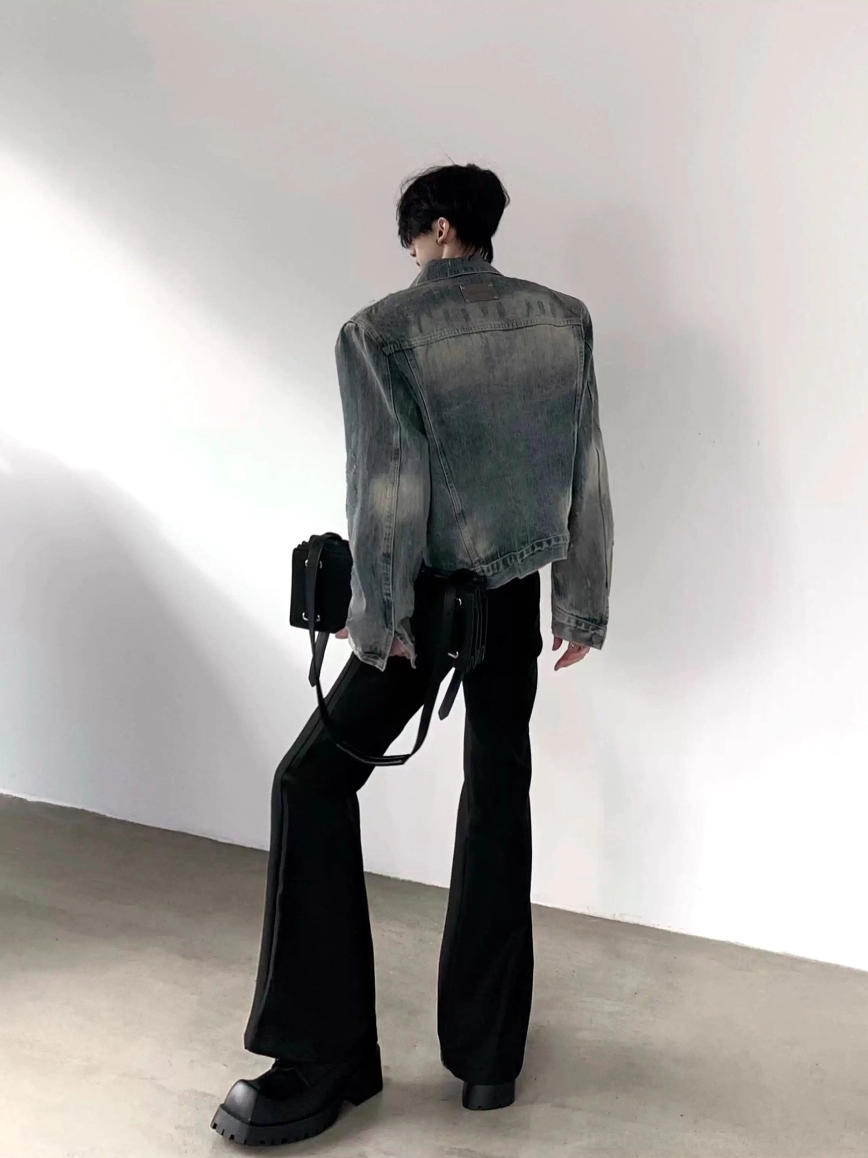 Back view of washed blue denim shoulder pad jacket showing faded vintage wash long sleeves and cropped streetwear silhouette