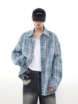 Model wearing a washed blue plaid overshirt with a white top, ripped jeans, and baseball cap in a relaxed oversized streetwear outfit