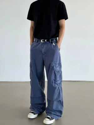 Back three-quarter view of washed blue wide-leg utility cargo pants styled with a black t-shirt, leather belt, and canvas sneakers