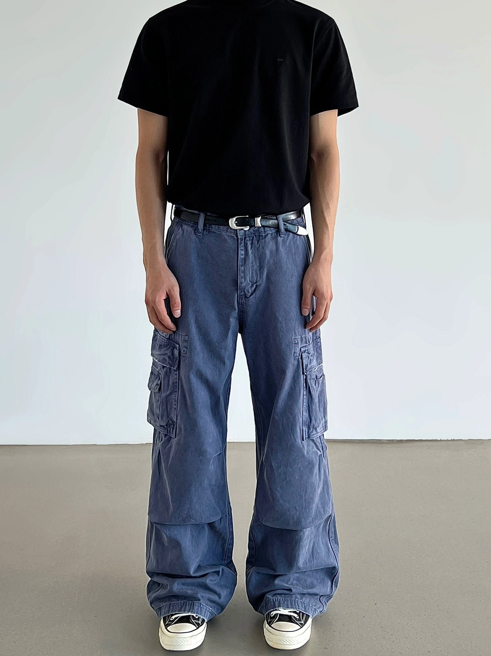 Front full view of loose washed blue cargo pants with wide straight legs, thigh flap pockets, black t-shirt, and sneakers