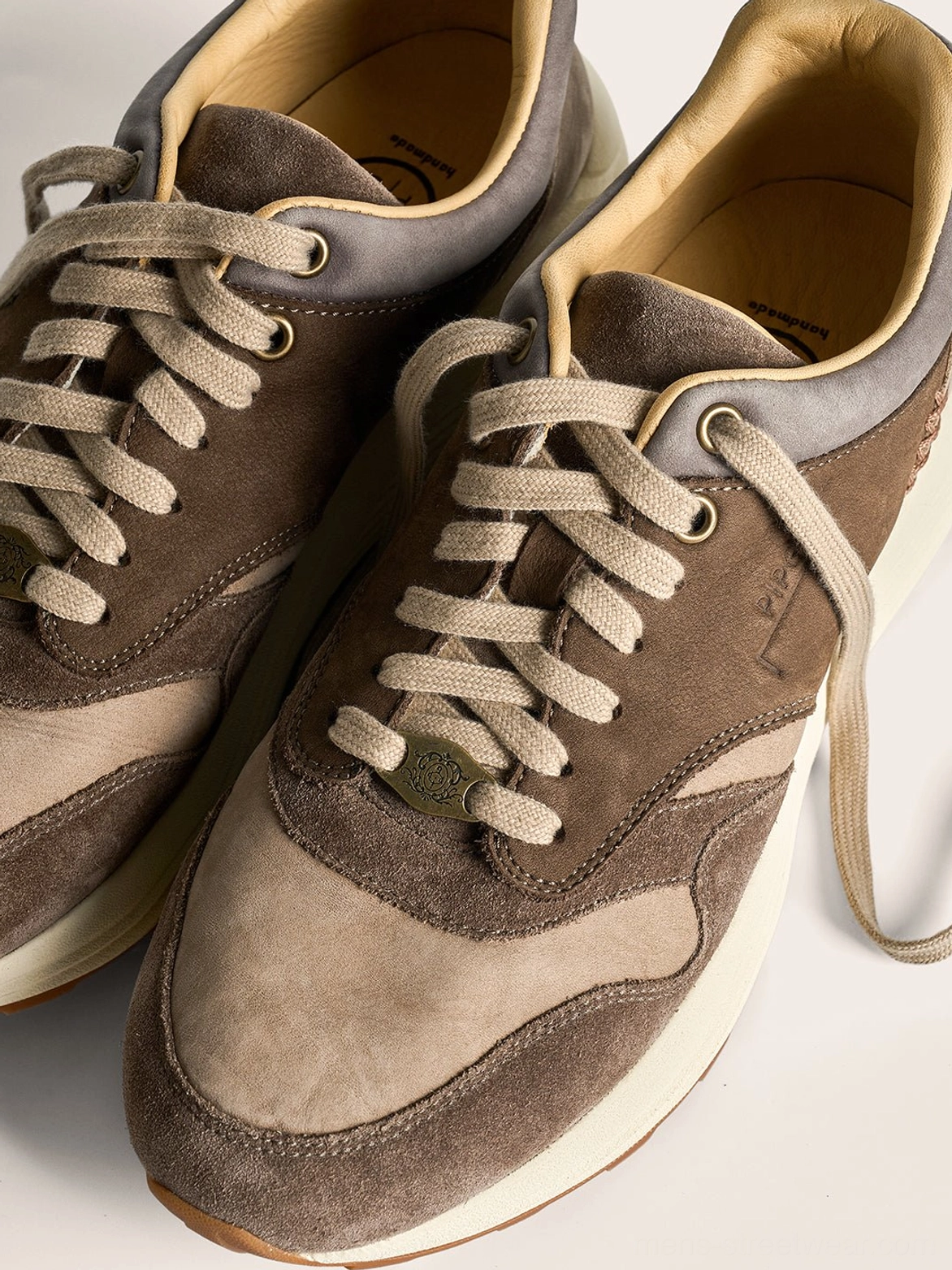 Pair of two-tone brown suede retro trail runner sneakers with matching laces and a low-top unisex silhouette