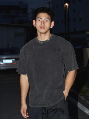 Washed black cotton oversized T-shirt with subtle chest lettering and relaxed crew neck styled on a male model in an urban night street setting