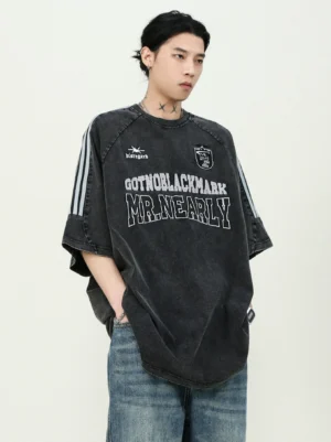 Model wearing an oversized carbon black washed crest varsity jersey T-shirt with triple sleeve stripes and wide-leg blue jeans