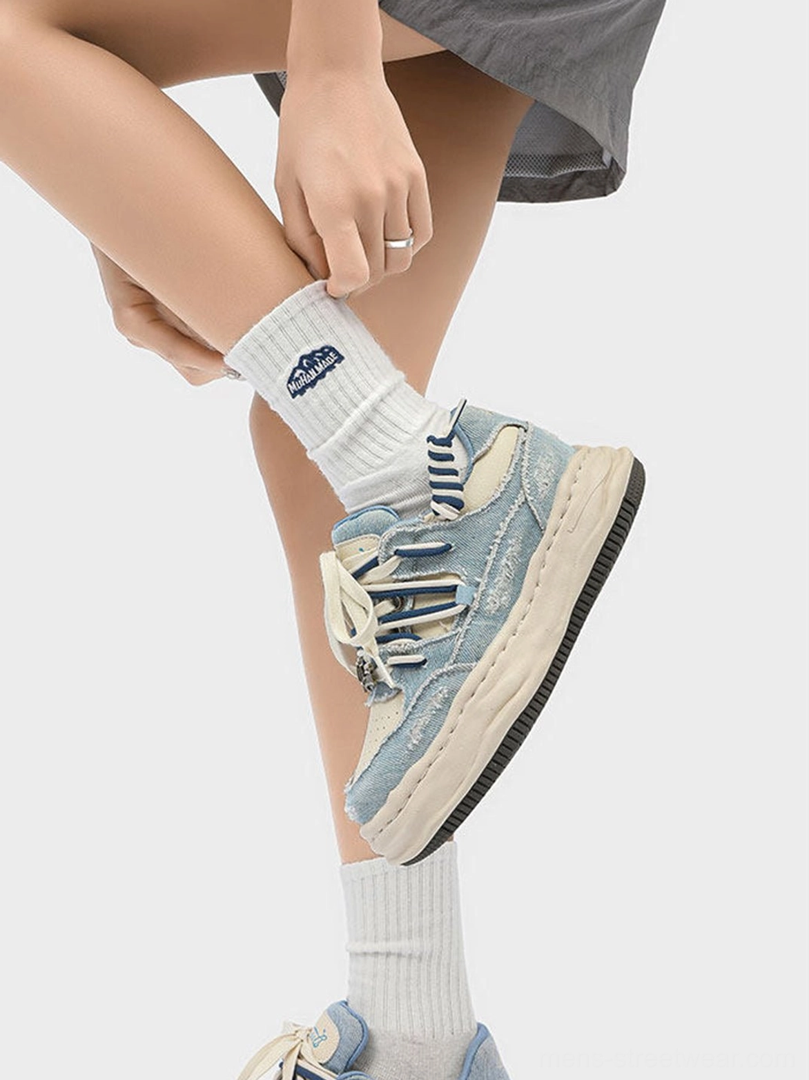 Close side view of washed denim dual-lace chunky streetwear sneaker showing distressed textile texture and striped laces