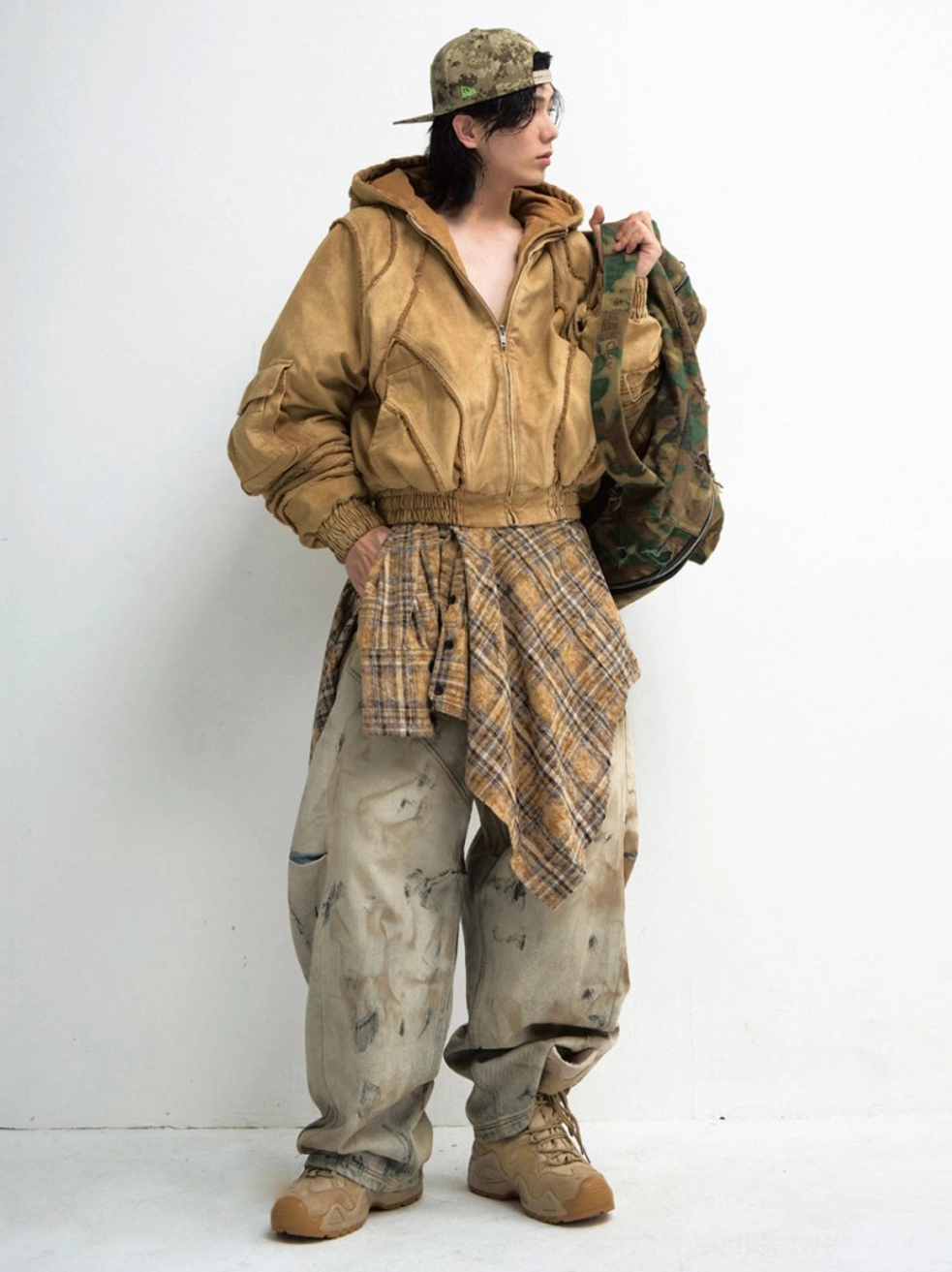 Distressed wide-leg cargo jeans side-front view styled with khaki work jacket plaid waist layer and camouflage bag