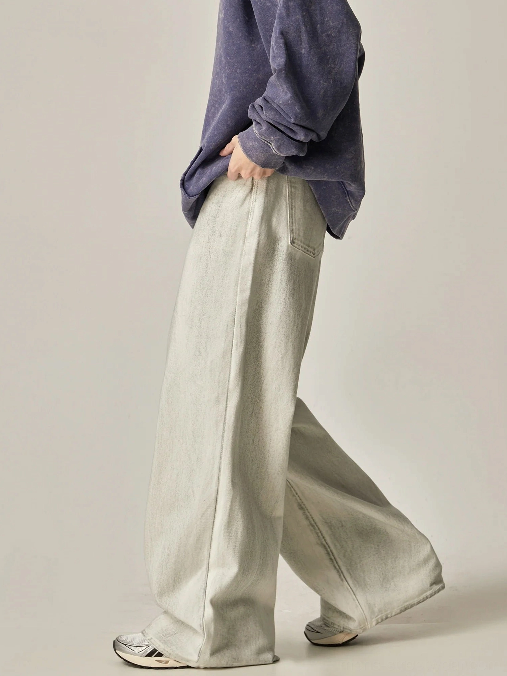 Walking side view of faded ecru wide-leg jeans with flared hem styled over retro running sneakers