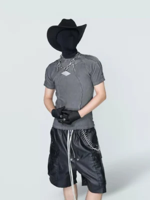 Front styling view of washed gray fitted streetwear T-shirt with sculpted exposed stitching, silver chain necklace, leather cargo shorts, and minimalist studio background