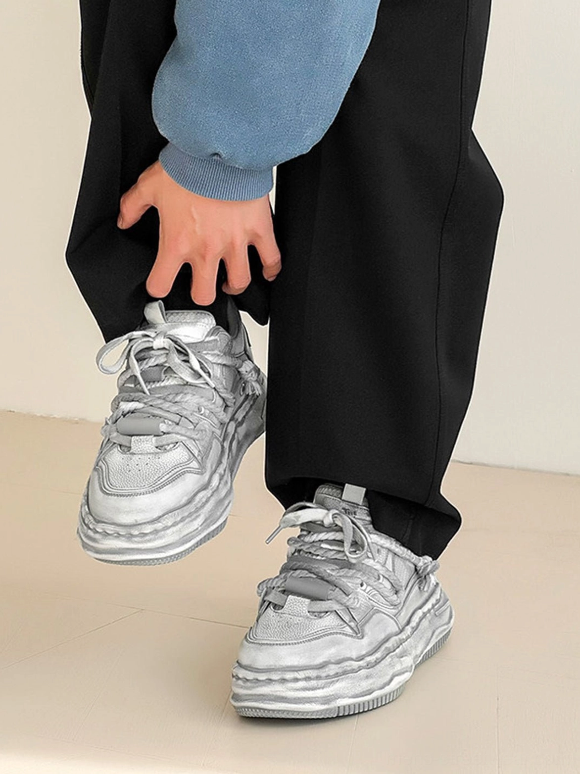 Washed gray platform sneakers worn with black pants and a blue cropped sweatshirt showing the side profile and elevated sole