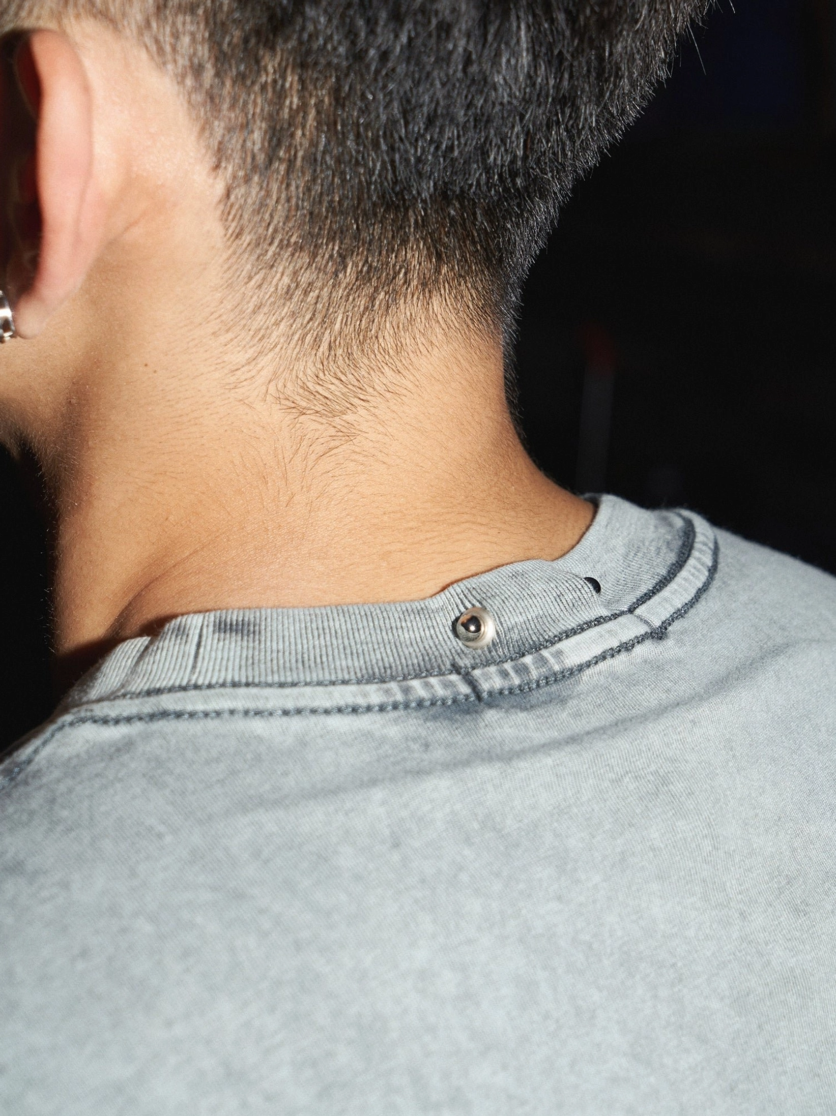 Washed grey cotton oversized T-shirt back neckline close-up showing faded finish, exposed collar button detail, and frayed ribbed crew neck trim