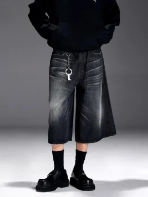 Close up view of washed grey black denim Bermuda shorts with wide culotte legs metal keychain detail and black streetwear styling