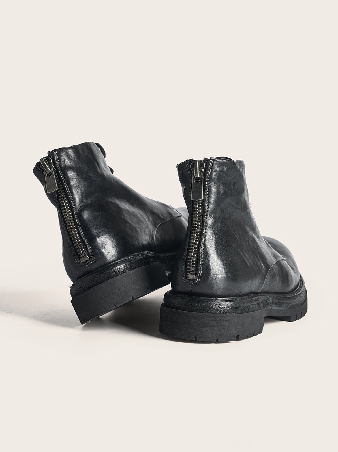 Rear three-quarter view of black washed horsehide combat boots with exposed metal back zippers and stacked lug heels