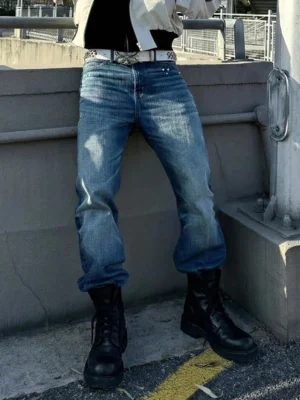 Model wearing black washed horsehide rear-zip combat boots with blue denim jeans on a concrete overpass