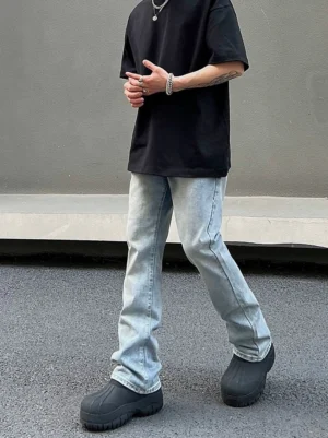 Male model wearing ice blue washed flared straight leg cargo jeans with a black T-shirt and chunky black boots on a concrete street