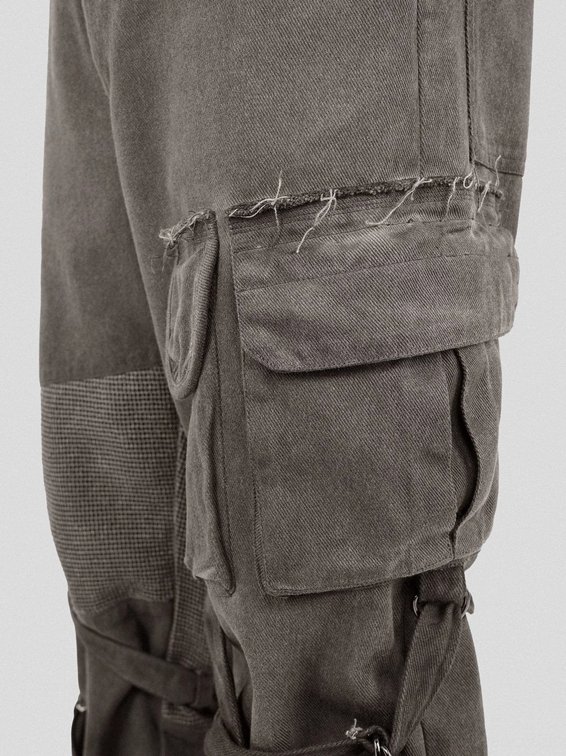Close-up oversized flap utility pocket on washed mesh tactical cargo pants with frayed edges and tactical leg straps