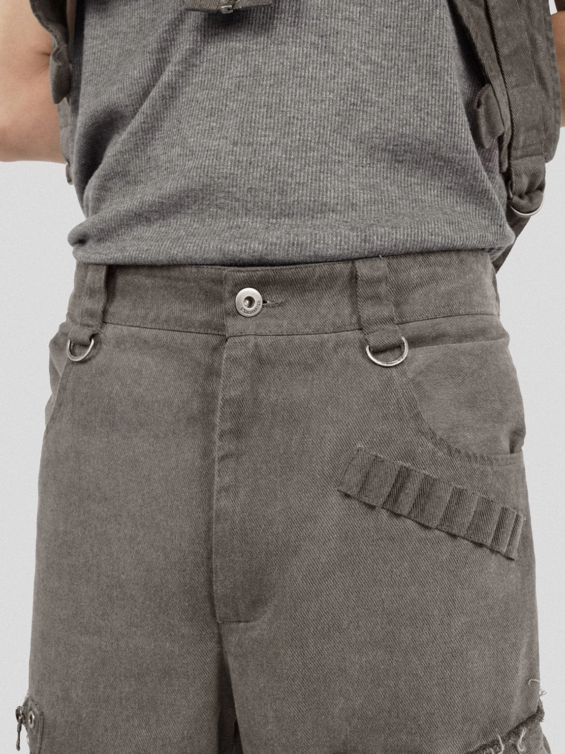 Close-up waistband detail of washed tactical cargo pants with metal button D-ring belt loop and distressed edge