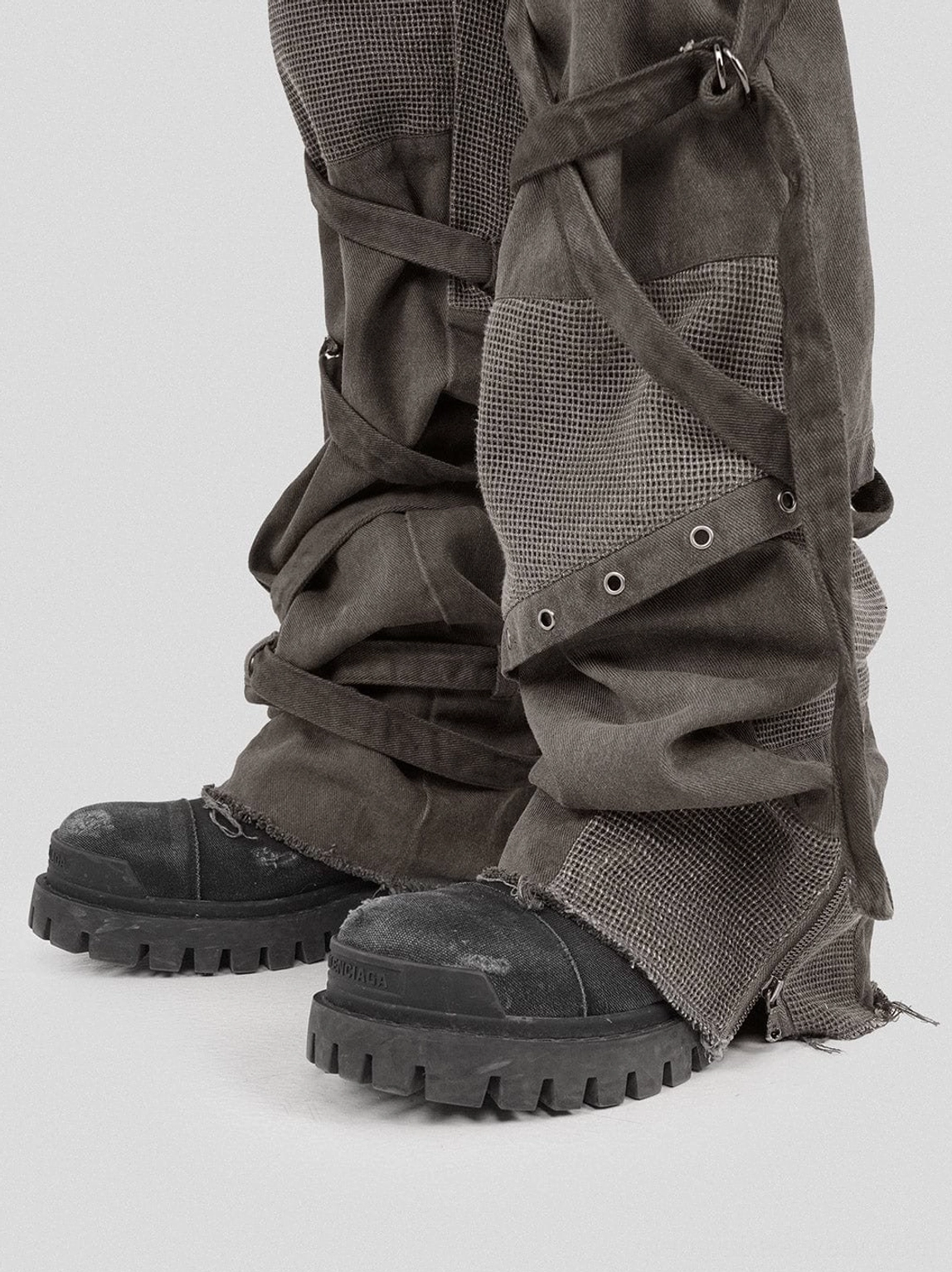 Dark grey washed mesh tactical cargo pants featuring wide legs utility pockets and industrial strap hardware