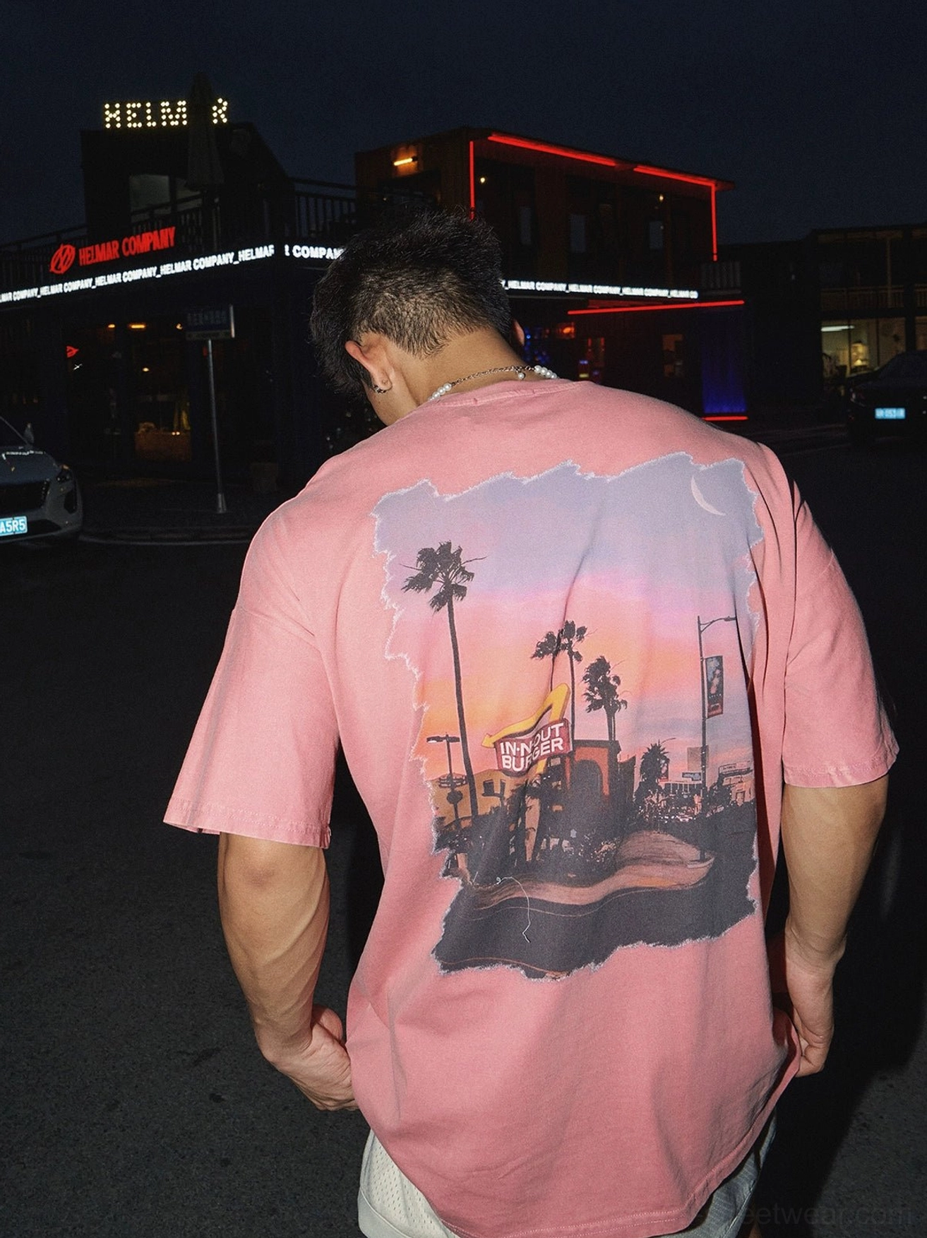 Back view of washed pink oversized streetwear t-shirt with distressed sunset diner and palm tree graphic worn by male model at night