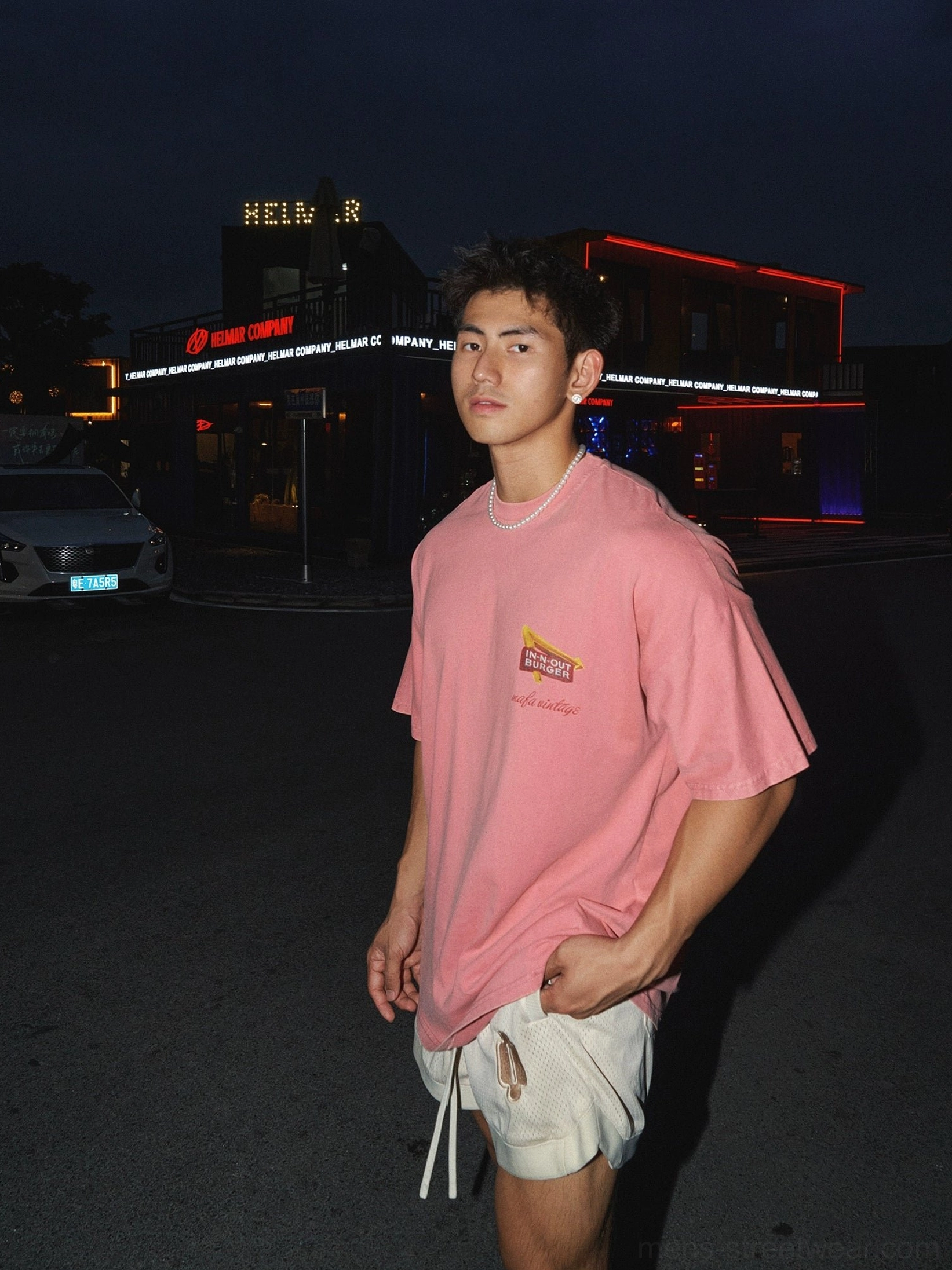 Front view of washed pink oversized crewneck graphic t-shirt with small retro diner chest logo on male model in night street setting