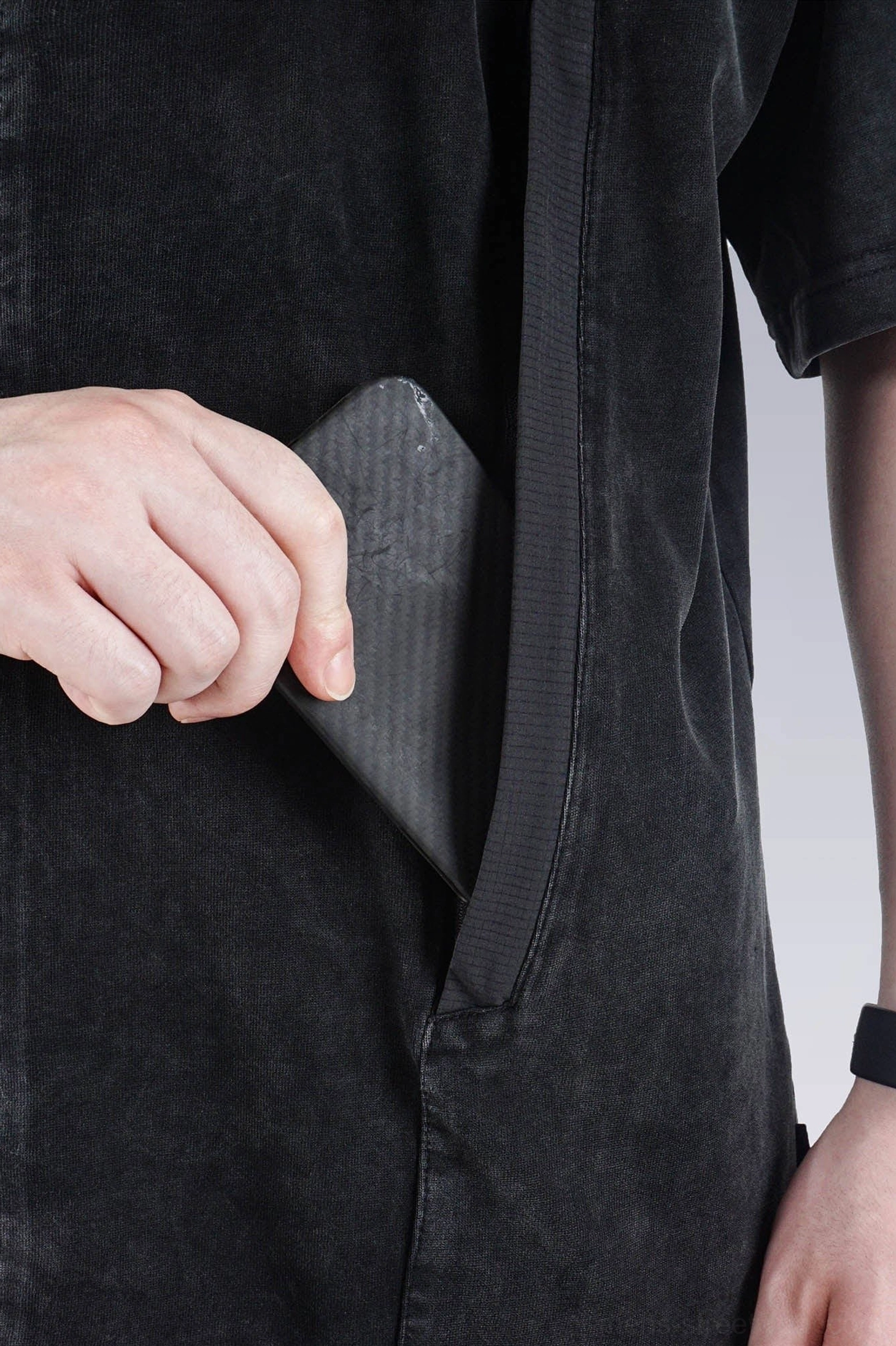 Close-up of faded black washed technical T-shirt hidden side seam pocket with reinforced opening and woven accent