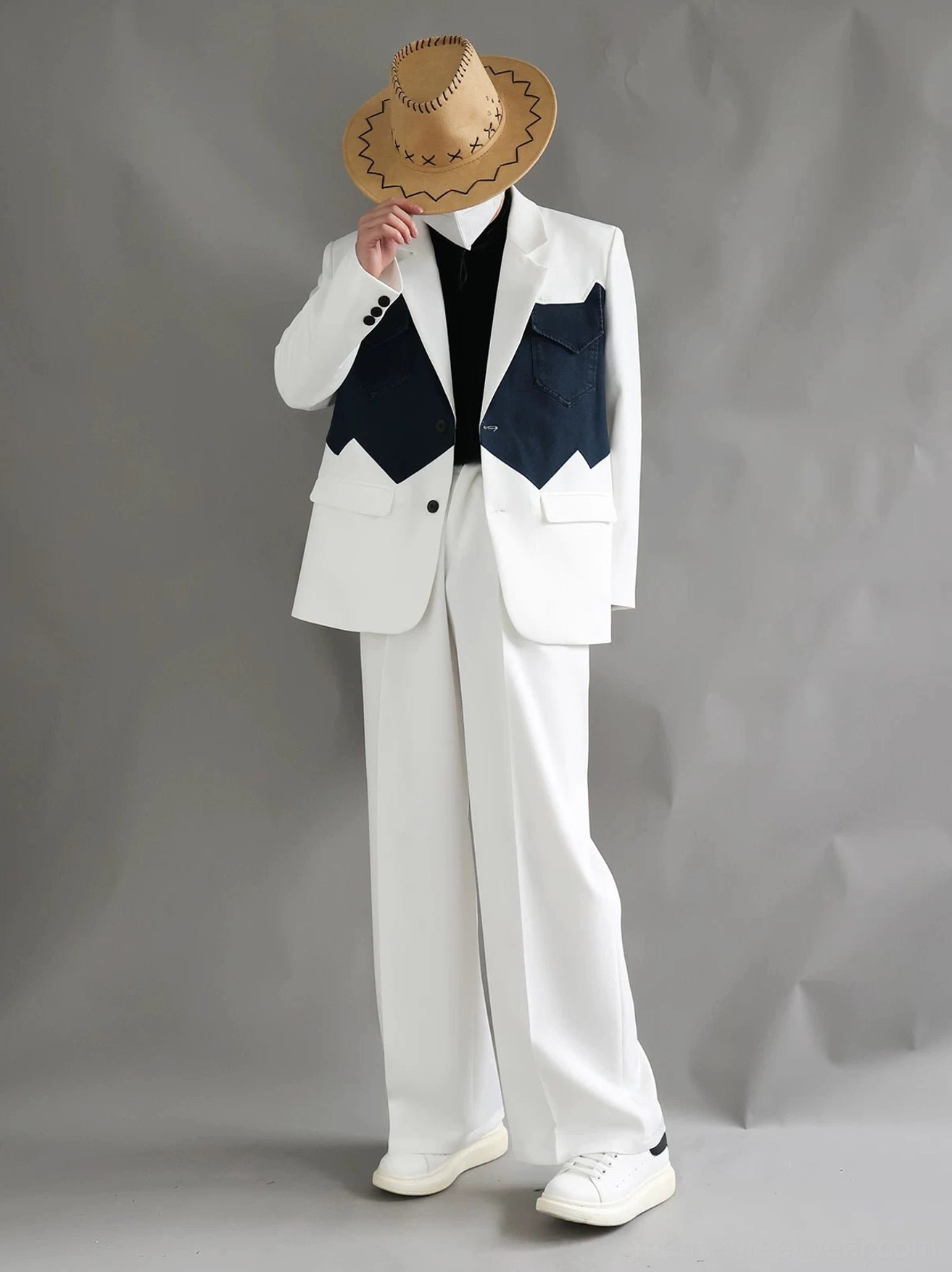 Streetwear styling of a two-tone Western suit with ivory blazer, navy pocket accents, wide-leg trousers, cowboy hat, and white sneakers