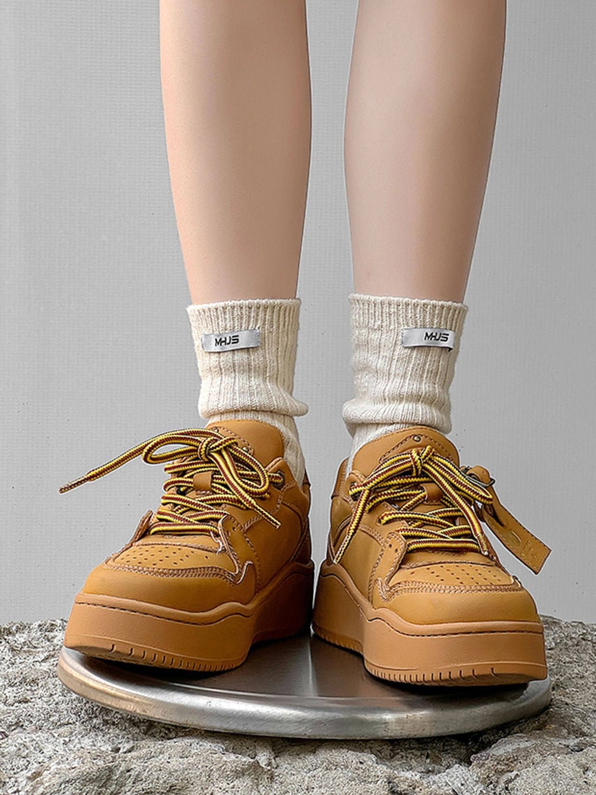 Wheat brown chunky platform sneakers worn with beige logo socks in a low angle rear view on concrete ground