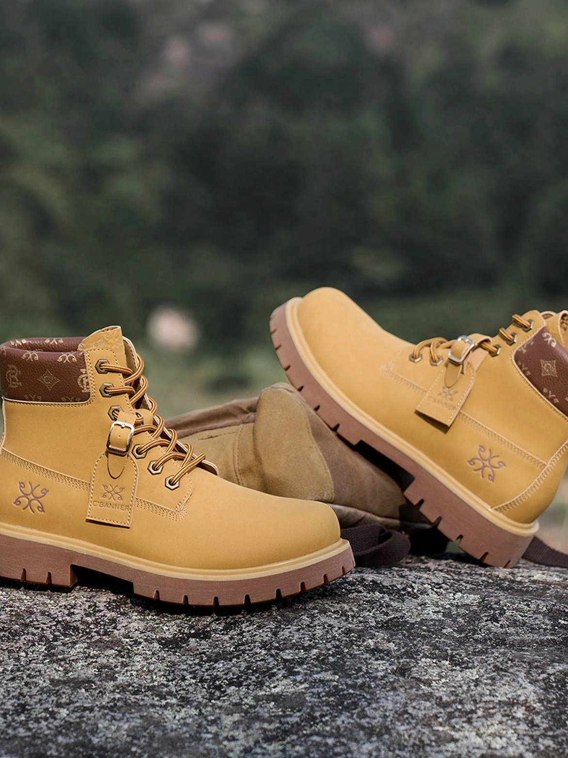 Wheat lace-up work boots arranged on an outdoor rock surface against a mountain forest background with contrasting brown collars