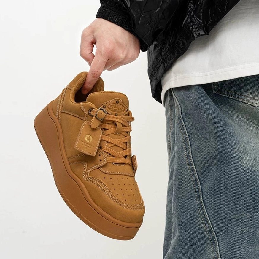 Wheat tan suede platform skate sneaker held by the tongue showing wide laces, leather tag, low-top shape and thick rubber sole