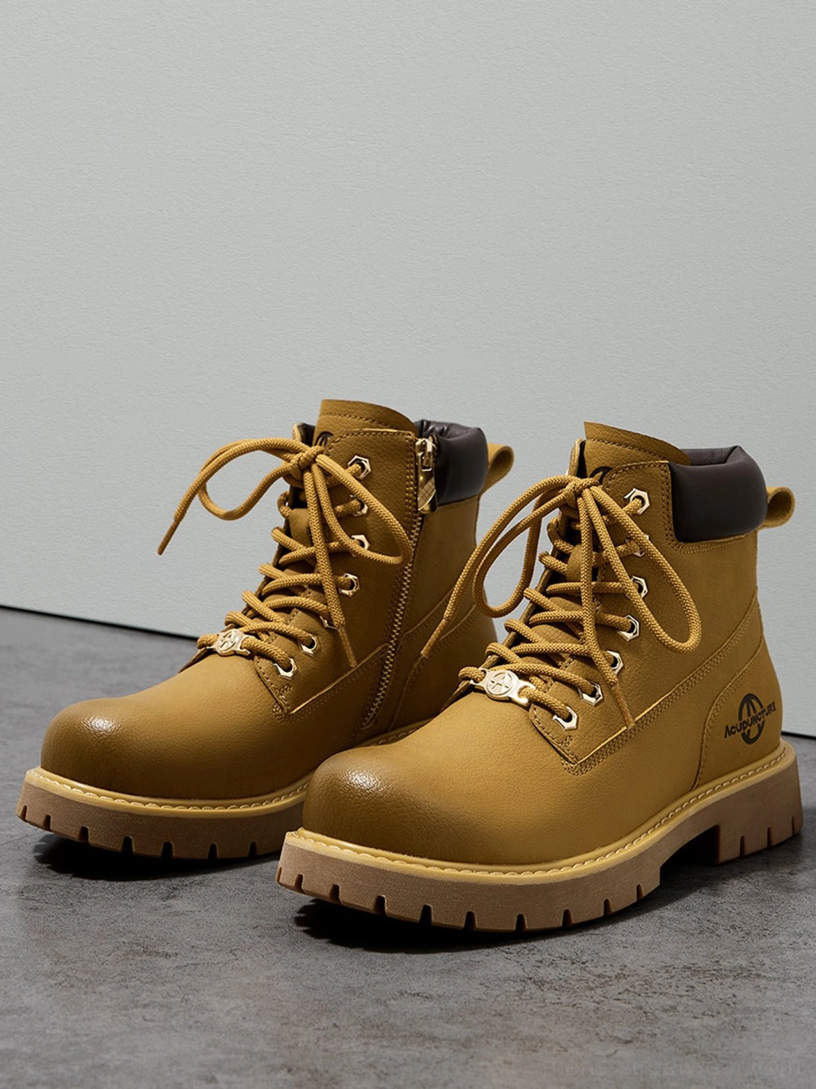 Pair of wheat yellow zip closure work ankle boots arranged on a minimalist concrete floor