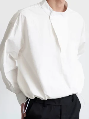 White asymmetric stand collar shirt for men in relaxed Korean streetwear fit, shown from the front with chest pocket and drawstring hem