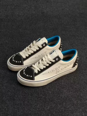 White blue-trim pearl-studded low-top skate sneakers shown from a three-quarter side angle with black suede-style toe caps, blue lining, and silver embellishments