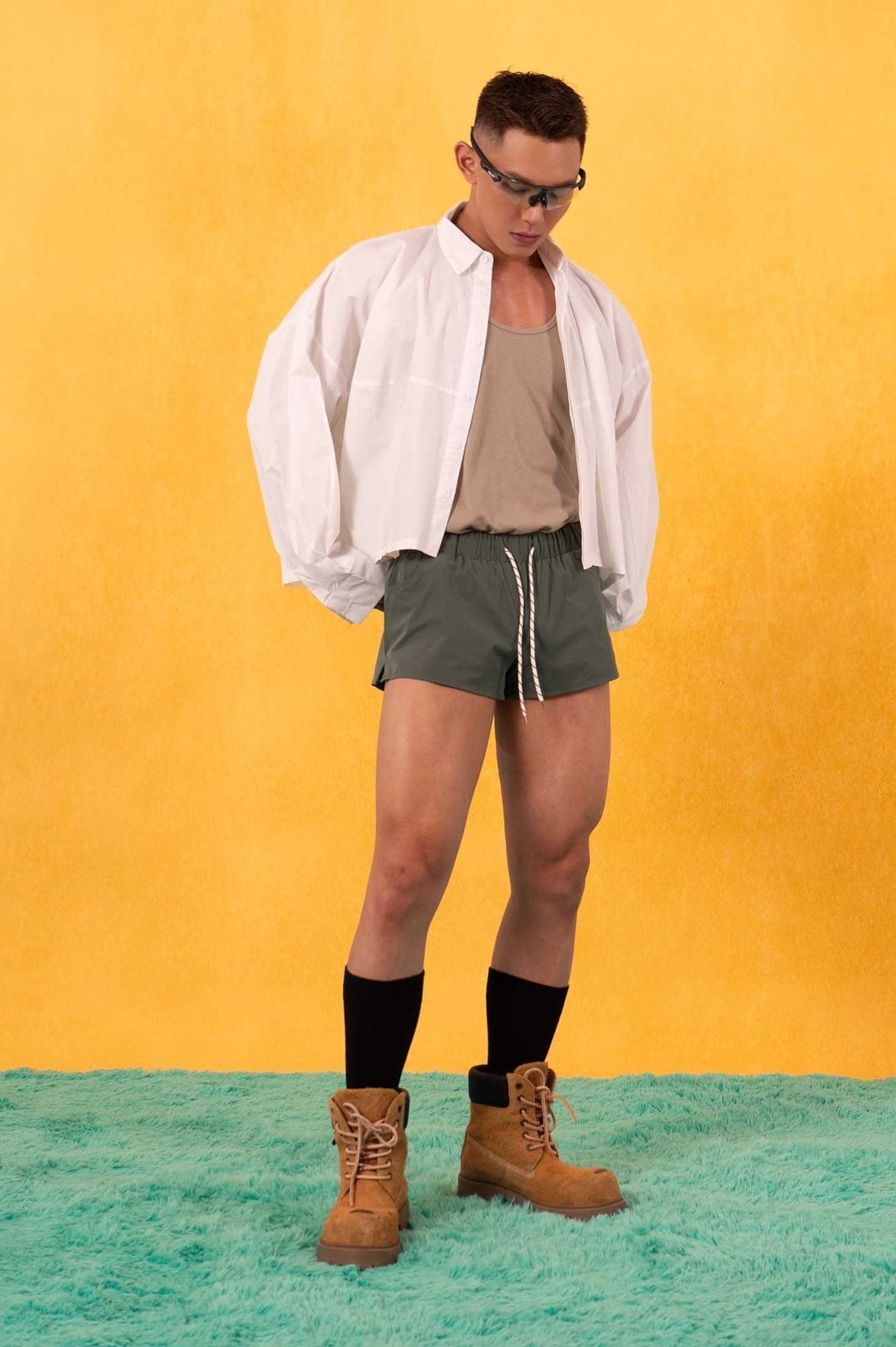 White oversized cropped cotton poplin shirt styled with a tank top, drawstring shorts, sunglasses, and work boots