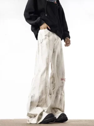 Side front view of white wide-leg streetwear jeans with grey brushstroke wash, distressed knee rip, relaxed oversized fit, and stacked hem worn with black platform sneakers