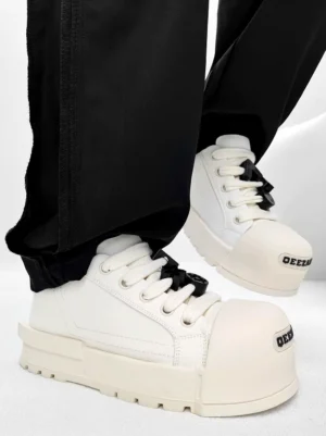 White chunky platform sneakers with black lace charms and square rubber toe cap worn with tailored black trousers