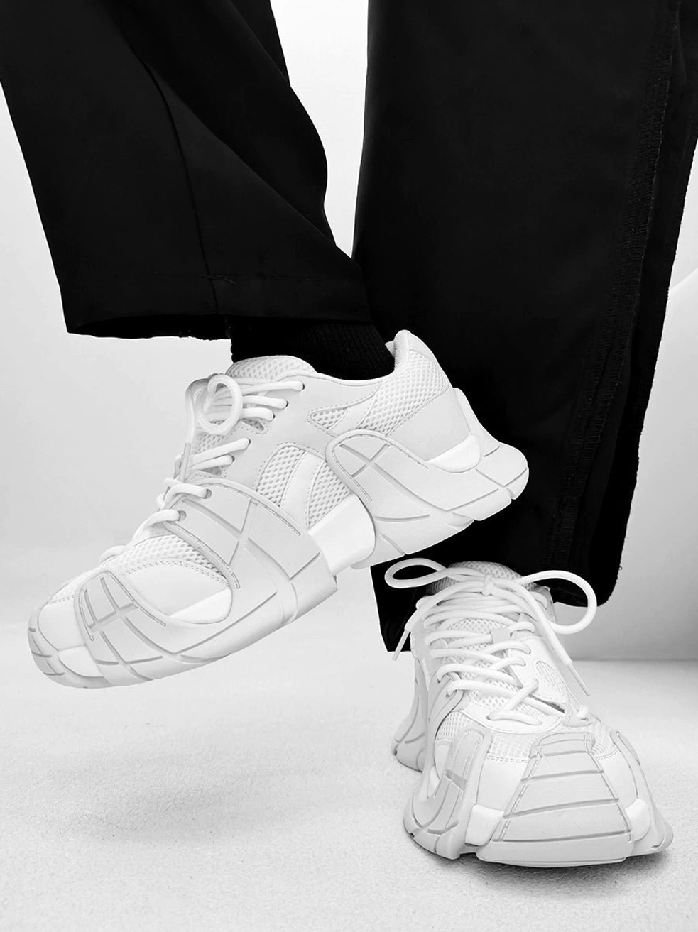 All-white futuristic chunky platform sneakers worn with relaxed black street pants, layered mesh upper, and thick segmented rubber outsole