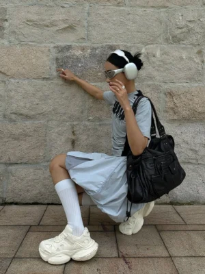 White chunky sneakers styled with a casual streetwear outfit, gray tee, light blue skirt, white socks, and silver sunglasses in an outdoor Seoul-inspired fashion setting