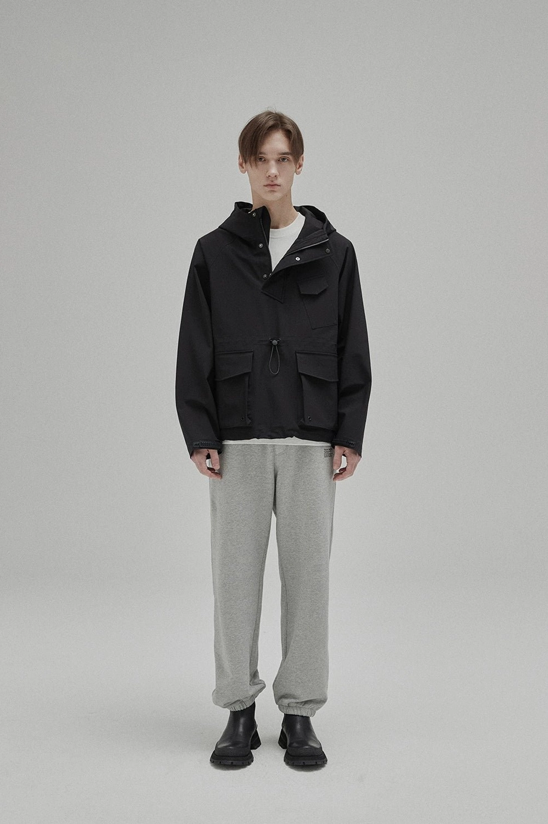 White minimalist cotton T-shirt layered under a black hooded cargo jacket with grey trousers and black boots