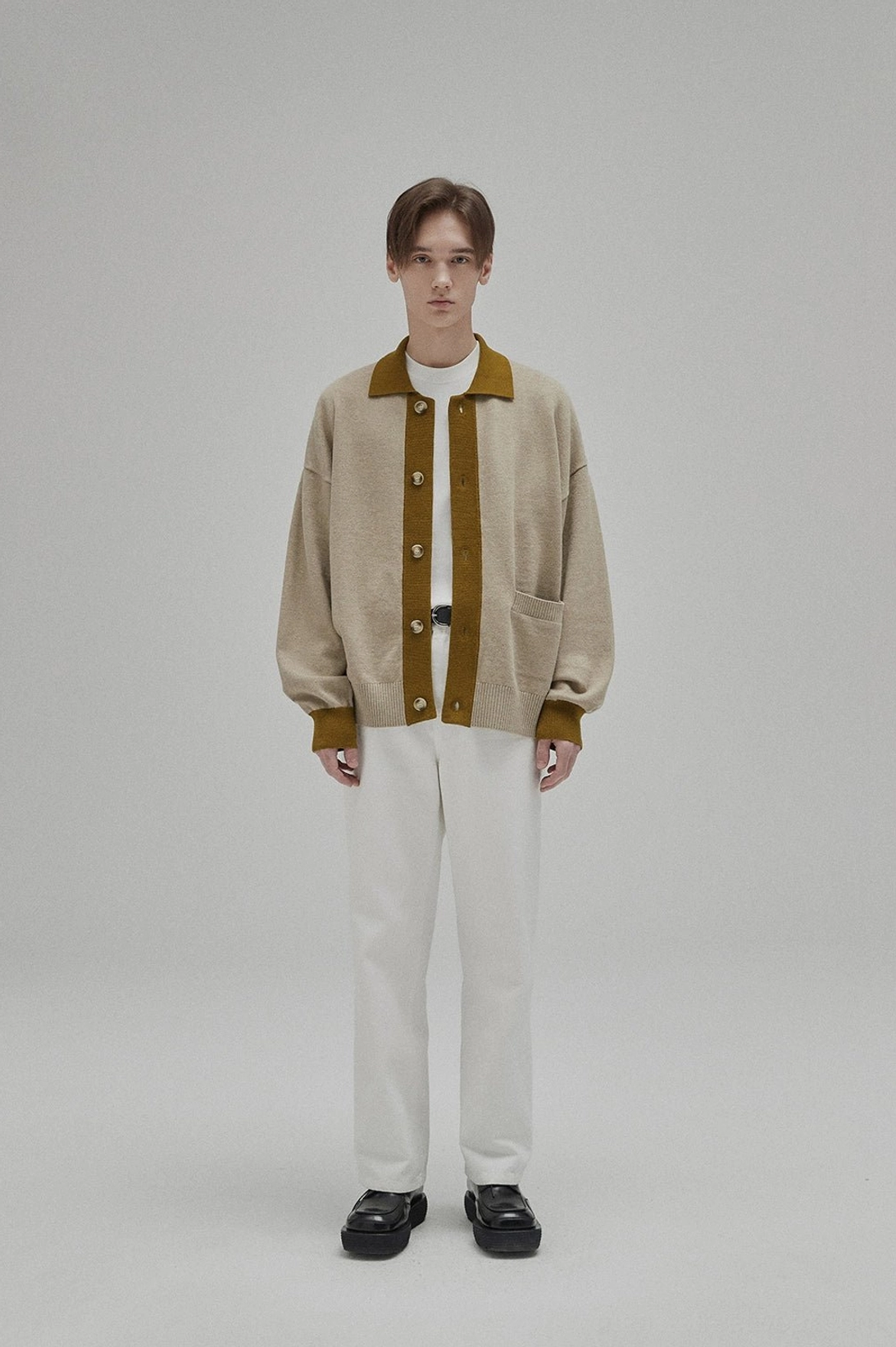 White minimalist crew neck T-shirt layered under a contrast trim knit cardigan with off-white trousers