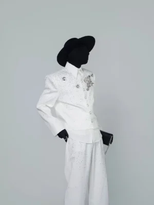 Three quarter view of a white crystal cropped jacket with silver rose applique styled over a white shirt with matching wide leg trousers
