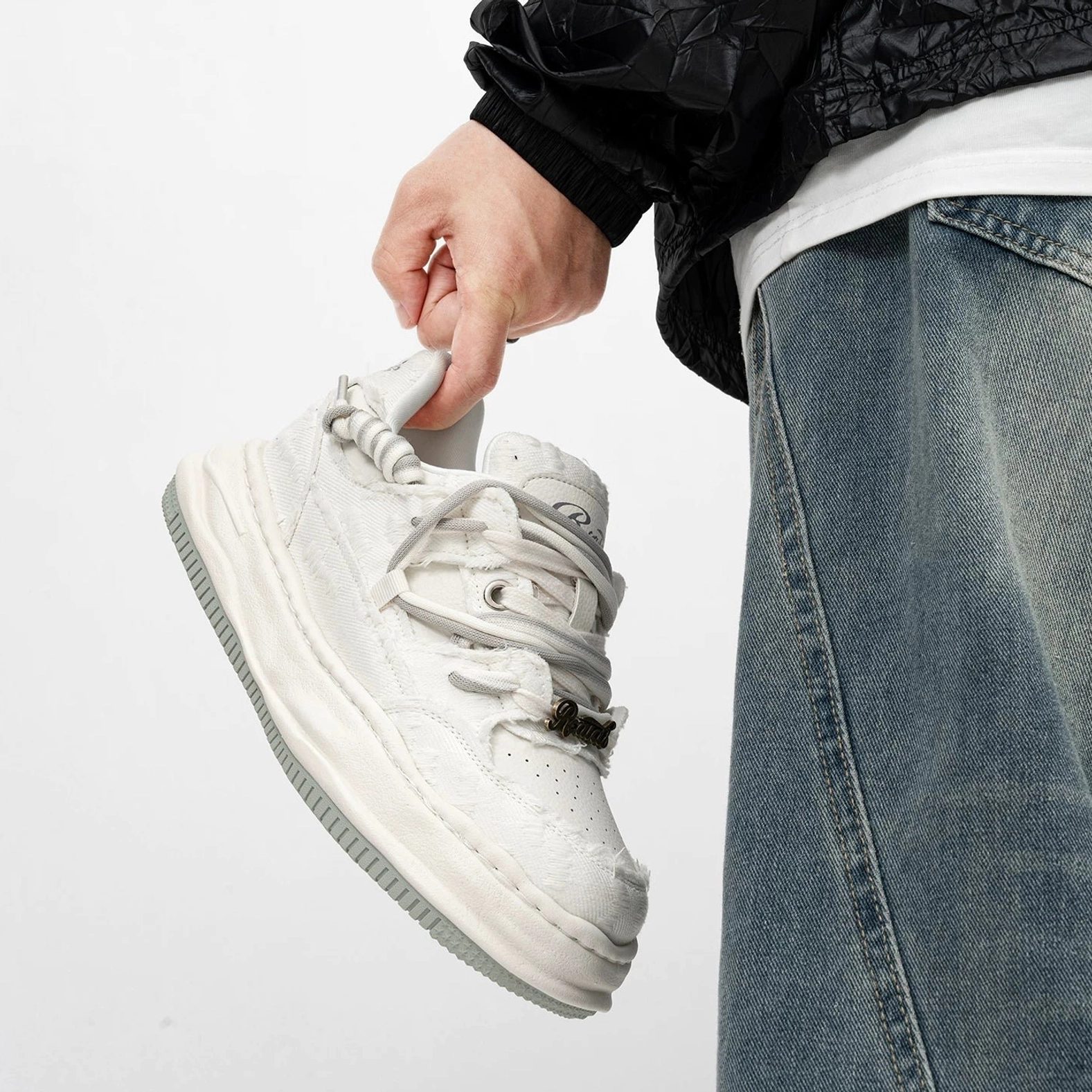 Three-quarter rear view of white distressed platform sneaker showing layered laces, metal lace tag, worn upper texture, and heel tab