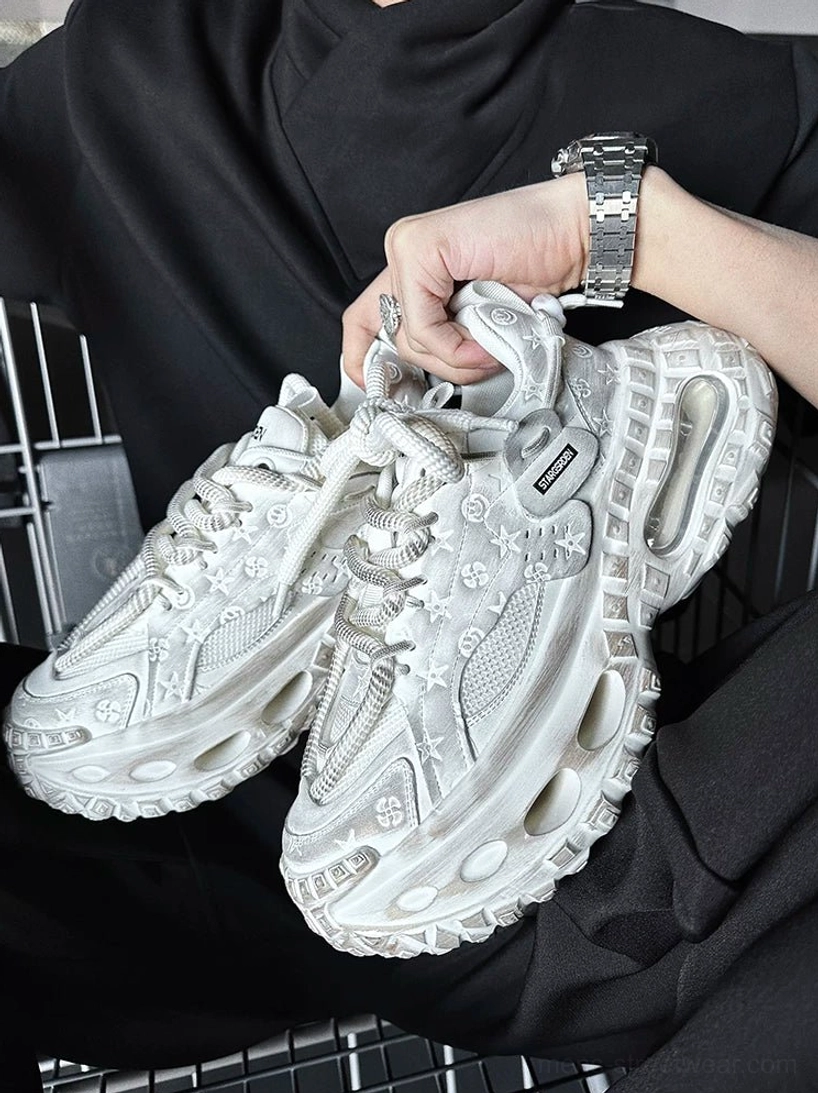 White distressed chunky platform sneaker held in hand showing embossed floral details, breathable mesh panels, thick laces, and futuristic rubber sole