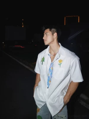 Side profile of a relaxed white embroidered streetwear shirt showing its loose drape and short sleeve silhouette styled with printed shorts