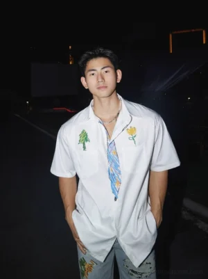 Front full-body view of a white doodle embroidered short sleeve shirt with colorful floral tree artwork patterned placket and chest pockets styled as Korean streetwear
