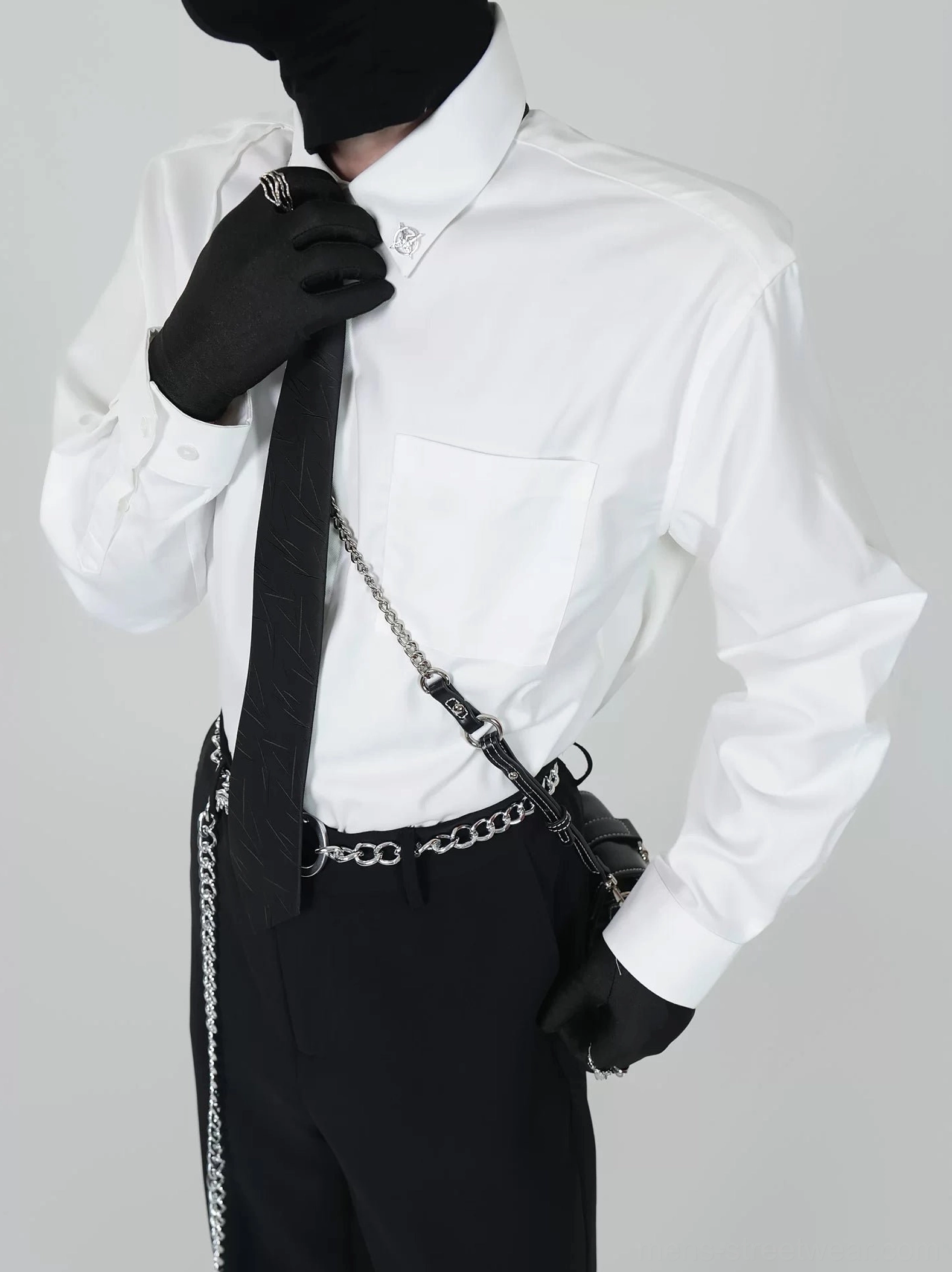 White dress shirt with textured black necktie and metallic collar pin detail styled with black gloves and silver chain accessories