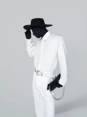 Three-quarter view of a white embellished button-up shirt and matching trousers with scattered sparkling studs, silver rhinestone belt, and black chain bag
