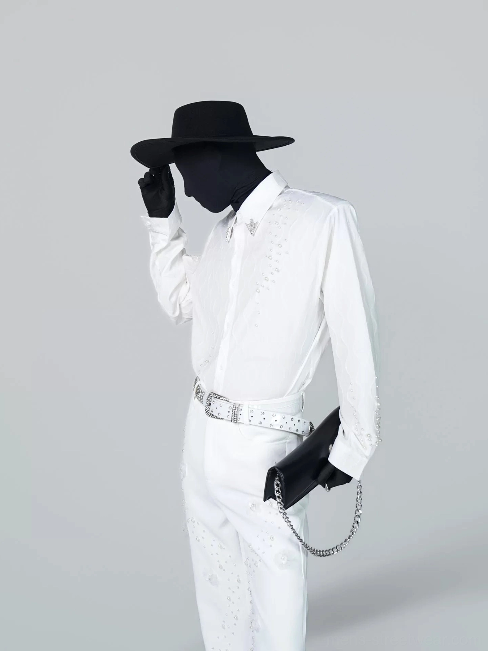 Three-quarter view of a white embellished button-up shirt and matching trousers with scattered sparkling studs, silver rhinestone belt, and black chain bag