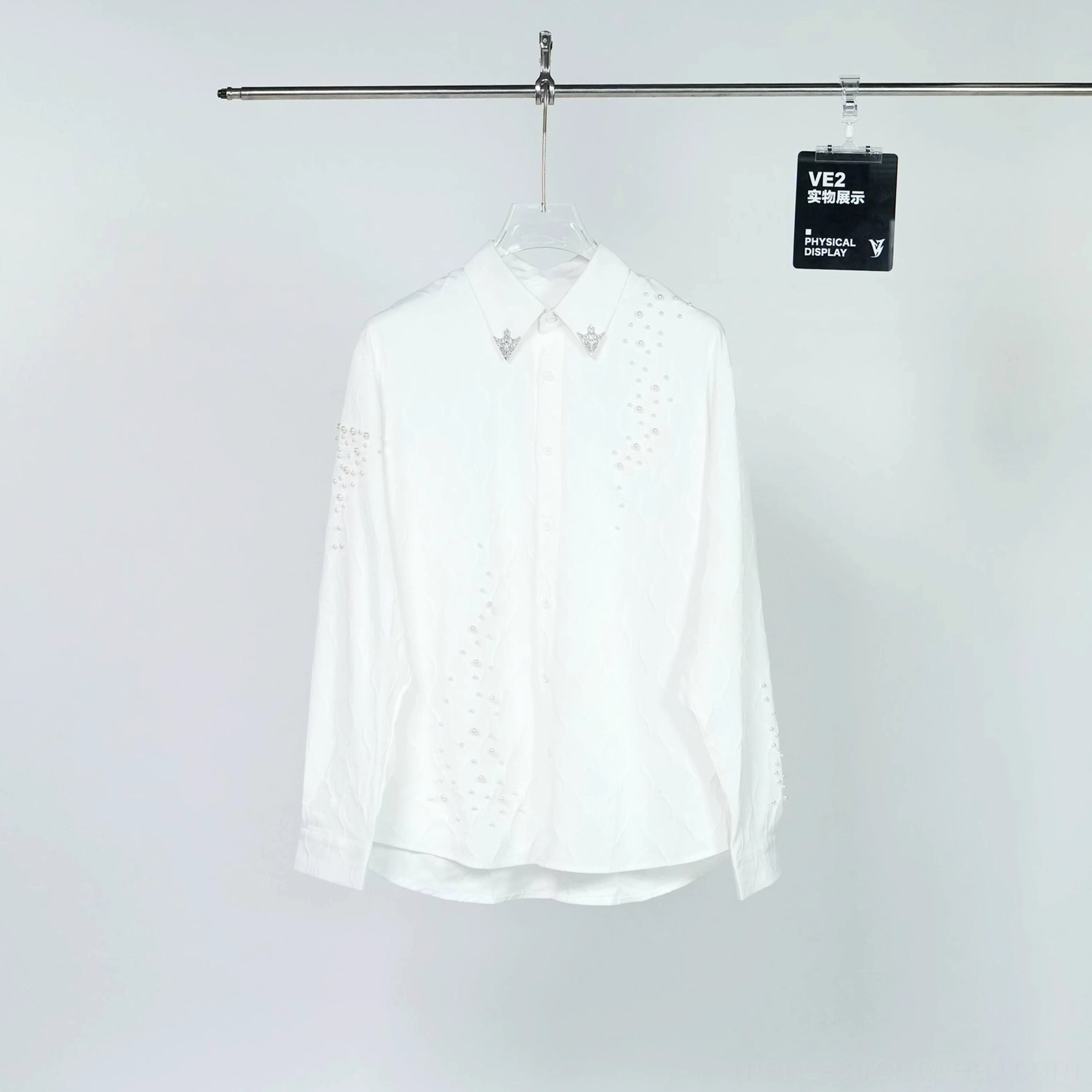 Front flat view of a white embellished long sleeve button-down shirt with pointed collar, silver star collar pins, textured fabric, and scattered sparkling studs