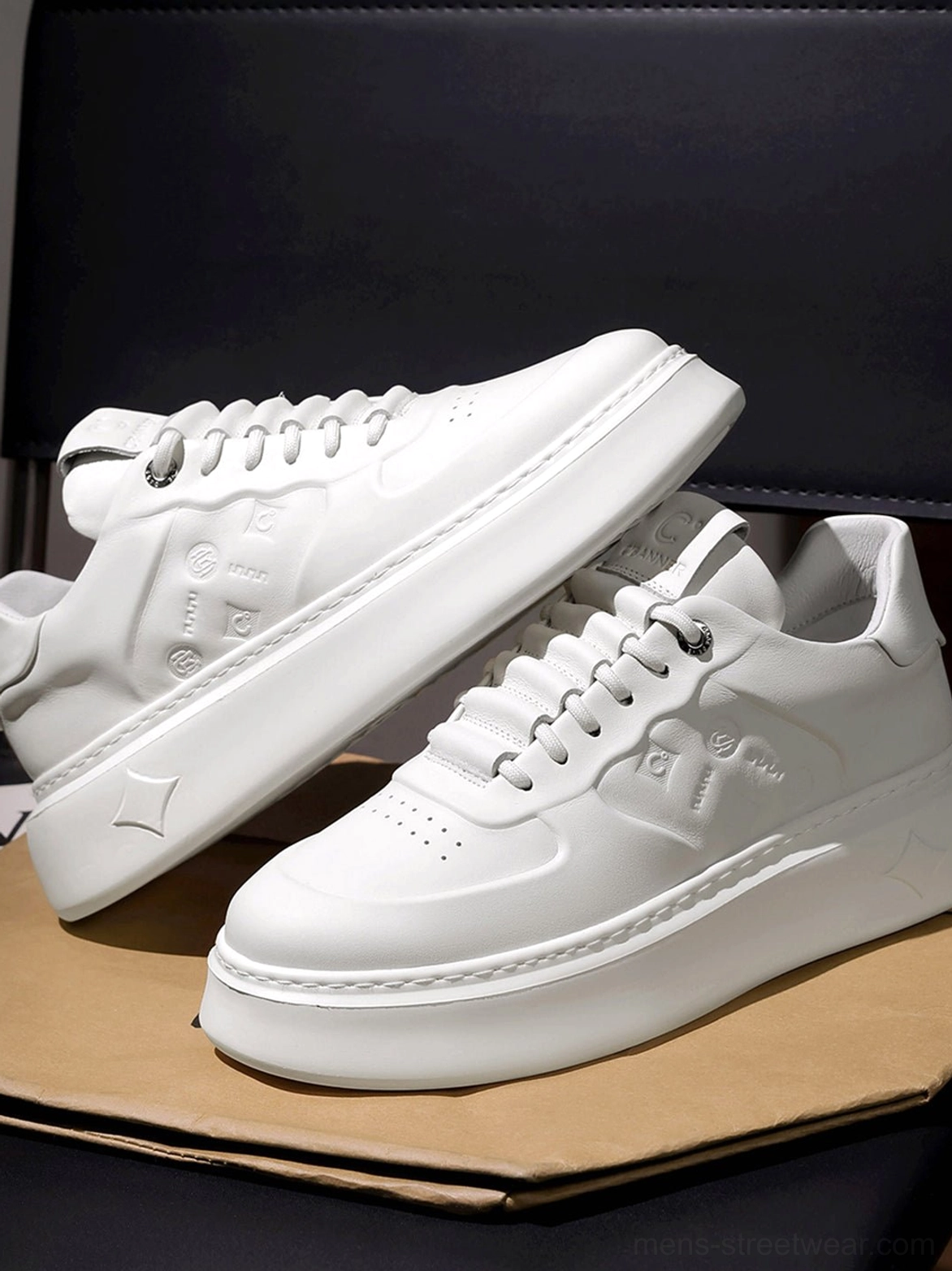 Close-up side flat lay of white chunky platform sneakers highlighting embossed monogram-style side panel texture